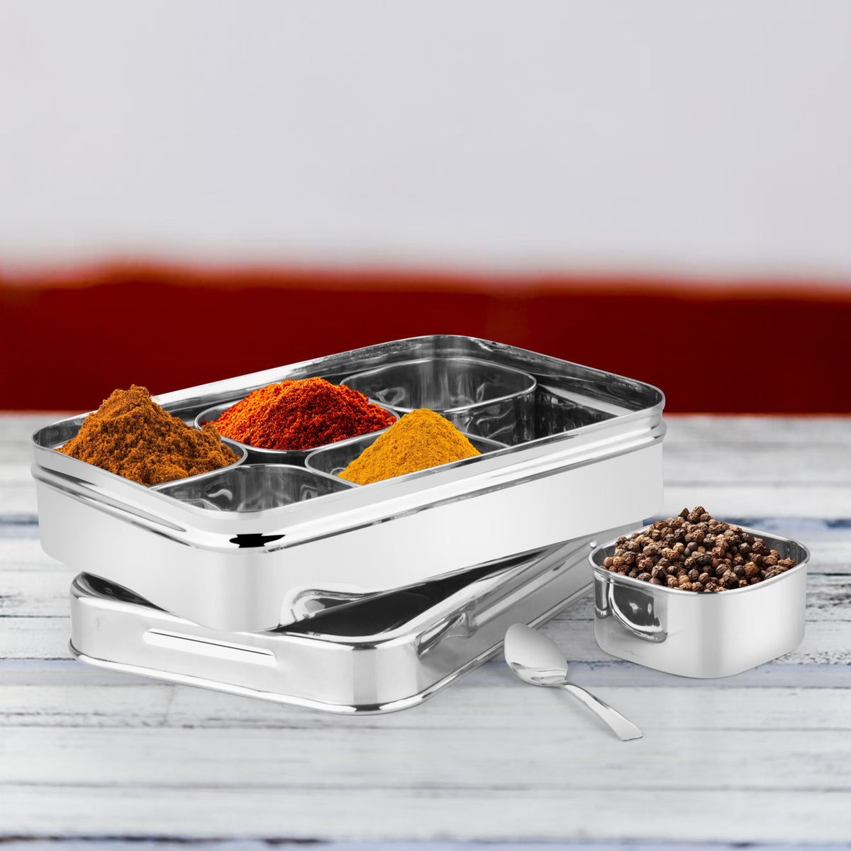 Close-up top view of a rectangle masala dabba showcasing vibrant Indian spices in round containers under a see-through lid.
