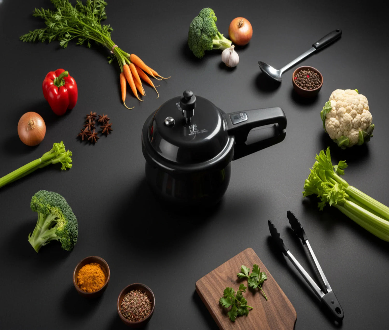 Modern Indian kitchen with a black pressure cooker, fresh vegetables, and spices on a dark countertop